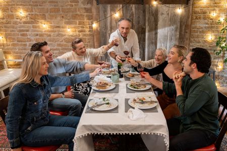 Scarlet Ireton, Antoni Porowski, Deborah Mackin, Clinton Pugh, Granny Pat, Florence Pugh, and Toby Sebastian cheers at the dinner table. (National Geographic/Chris Raphael)