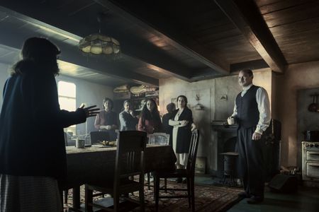 A SMALL LIGHT - The Gies, Frank, van Pels and Pfeffer families gather in the secret annex as seen in A SMALL LIGHT. (From left: Bel Powley as Miep Gies, Caroline Catz as Auguste van Pels, Noah Taylor as Dr. Pfeffer, Ashley Brooke as Margot Frank, Andy Nyman as Hermann van Pels, Amira Casar as Edith Frank, and Liev Schreiber as Otto Frank). (Credit: National Geographic for Disney/Martin Mlaka)