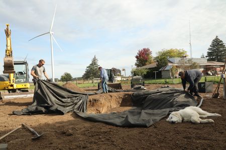 Scott Brady, Charles Pol, and Andrew Sutton lay out the pond liner in the hole they dug out for the new garden pond, while Clovis takes a nap in the dirt. (National Geographic)
