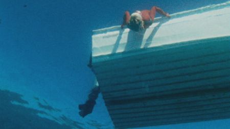 Valerie Taylor leaning over the boat looking into water in 1968. Shot from underwater.  (photo credit: Ron & Valerie Taylor)