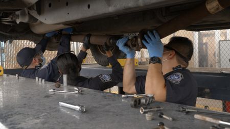 CBP Officers Thomas, Rodriguez, and Vasquez work together to dismantle the underside of a suspect's vehicle to retrieve smuggled narcotics in Pharr, Texas. (National Geographic)