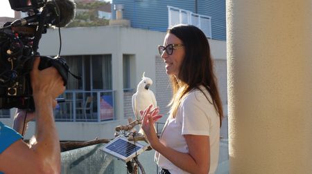 BTS of Suzy Roessel standing on her balcony with a cockatoo. (Big Wave Productions)