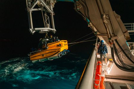 Crew Colin Wollerman stands on deck as the submarine is lifted out of the water at night. (National Geographic/Patrick Hopkins)