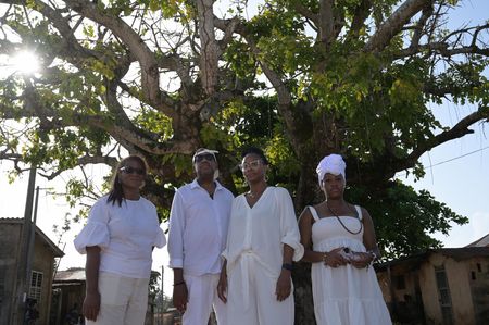 Clotilda descendants Cassandra Lewis, Garry Lumbers, Altevese Rosario, and Delisha Marshall stand together in front of The Tree of Return in Ouidah. (National Geographic/Etinosa Yvonne)