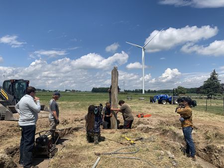 Evan Korthals and Tobias Edgett watch Ben Reinhold and Charles Pol place a wood beam to support the Pol family farm's sheep hut roof, while two crew members film them. (National Geographic)